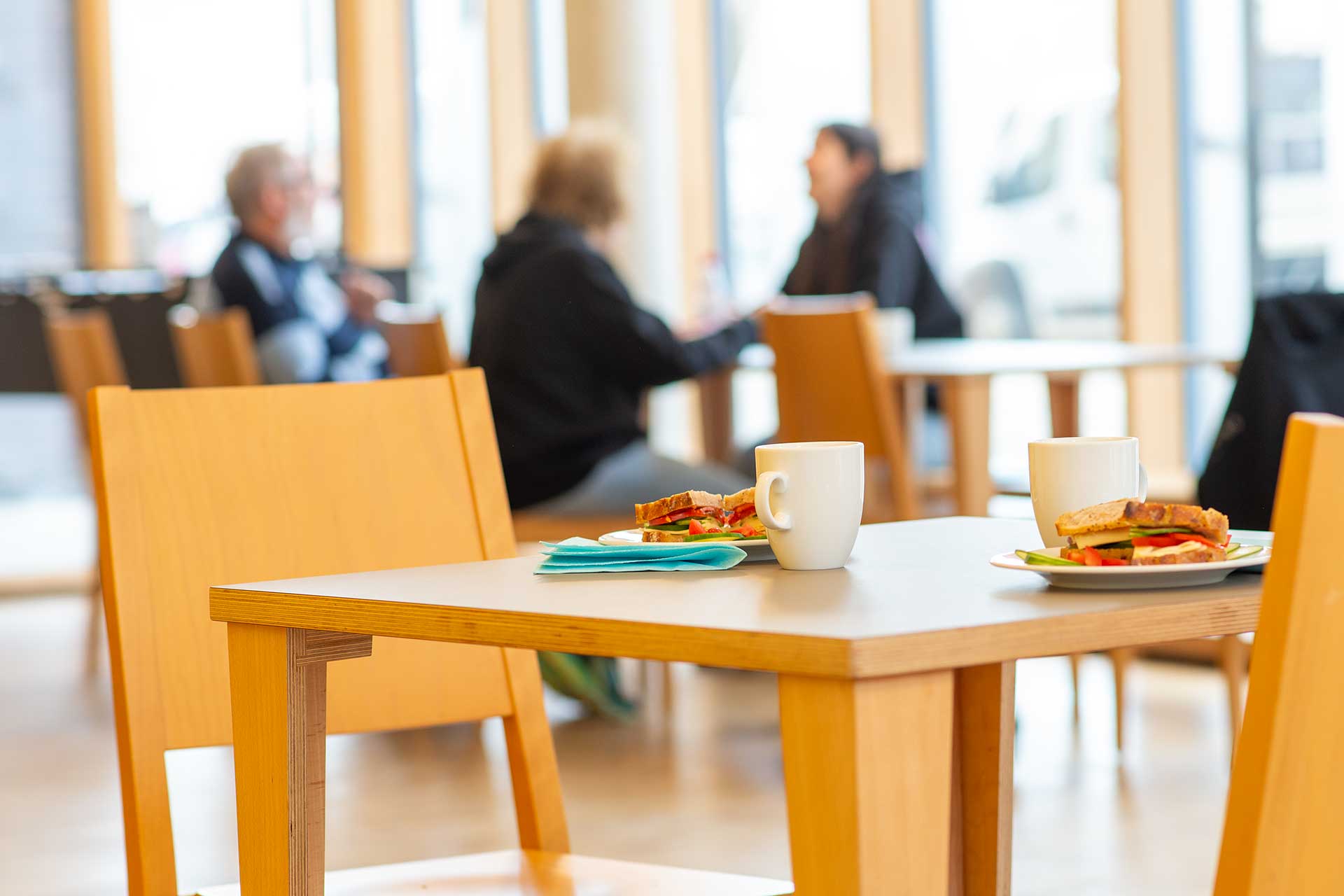 GPZ Ulm: helle Räumlichkeiten, im Hintergrund sitzen Menschen am Tisch essen und reden miteinander